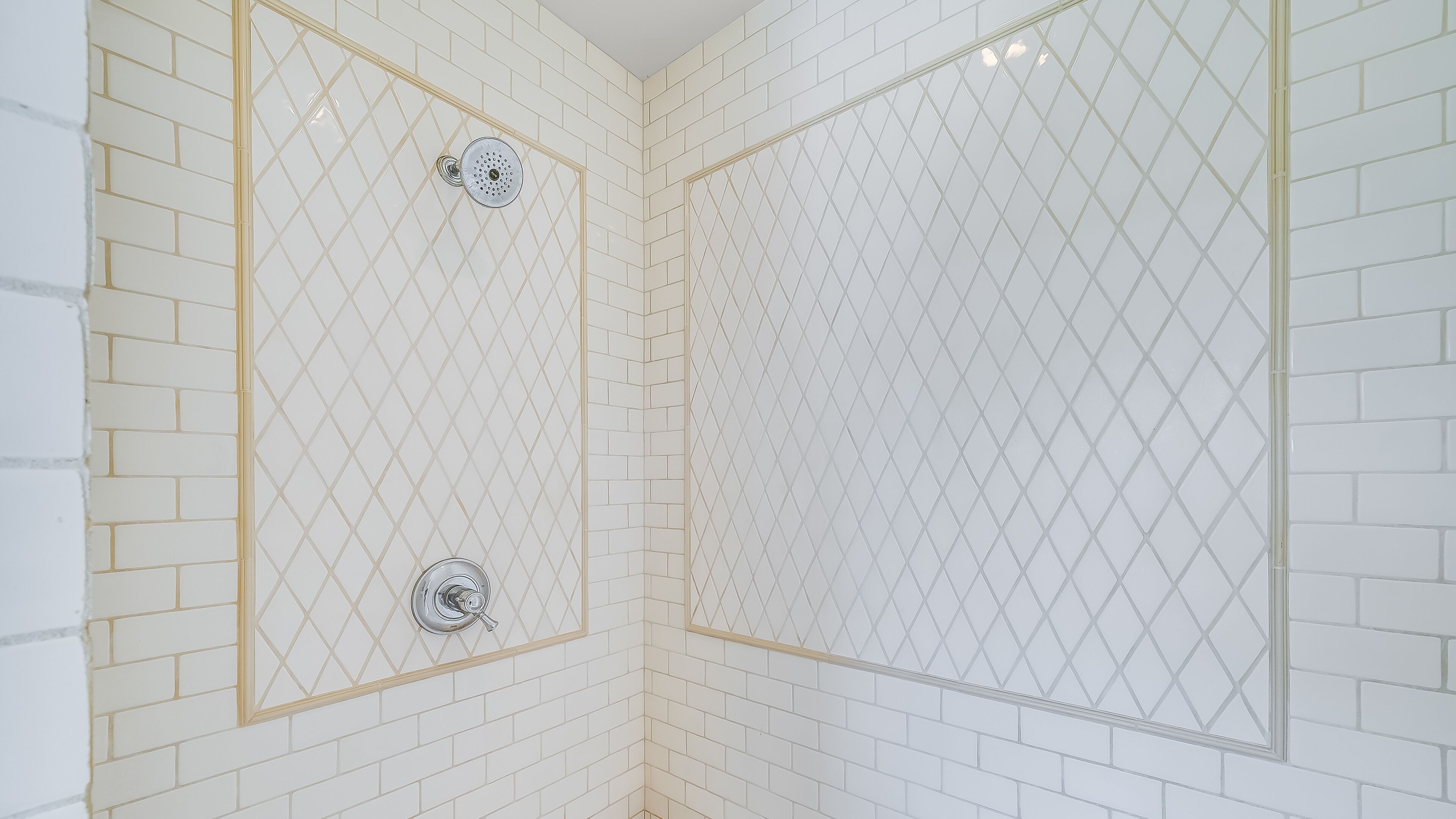 Una ducha con puerta de vidrio con diseño de rombos y un cabezal de ducha cromado.