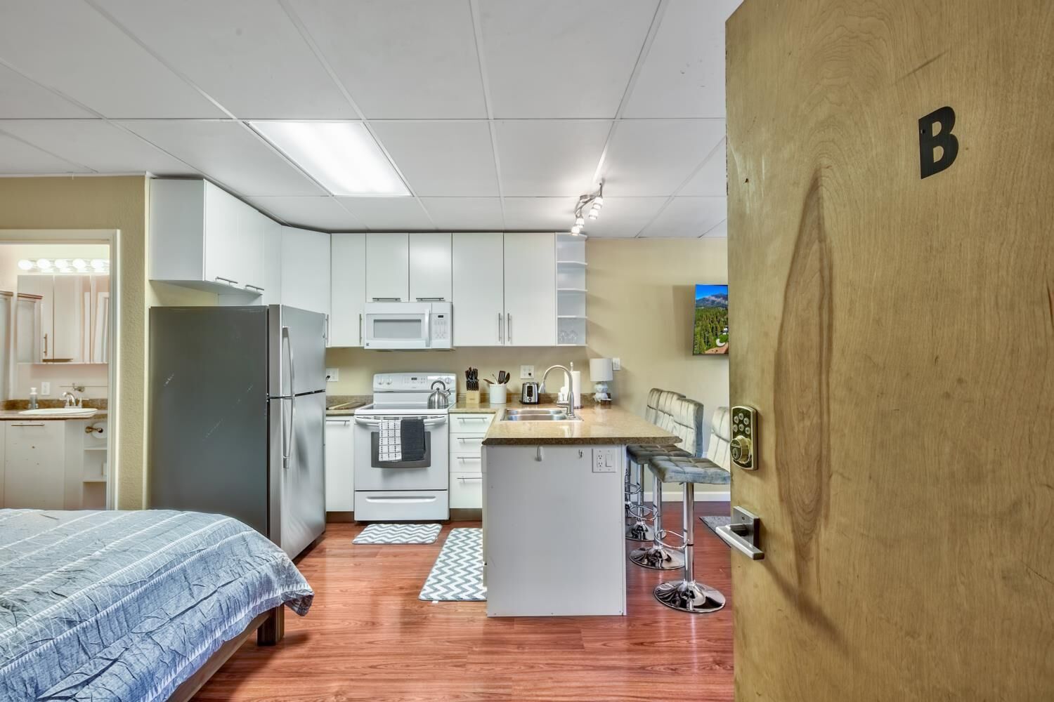 A compact kitchen with white cabinets, a refrigerator, a microwave, and a stove.