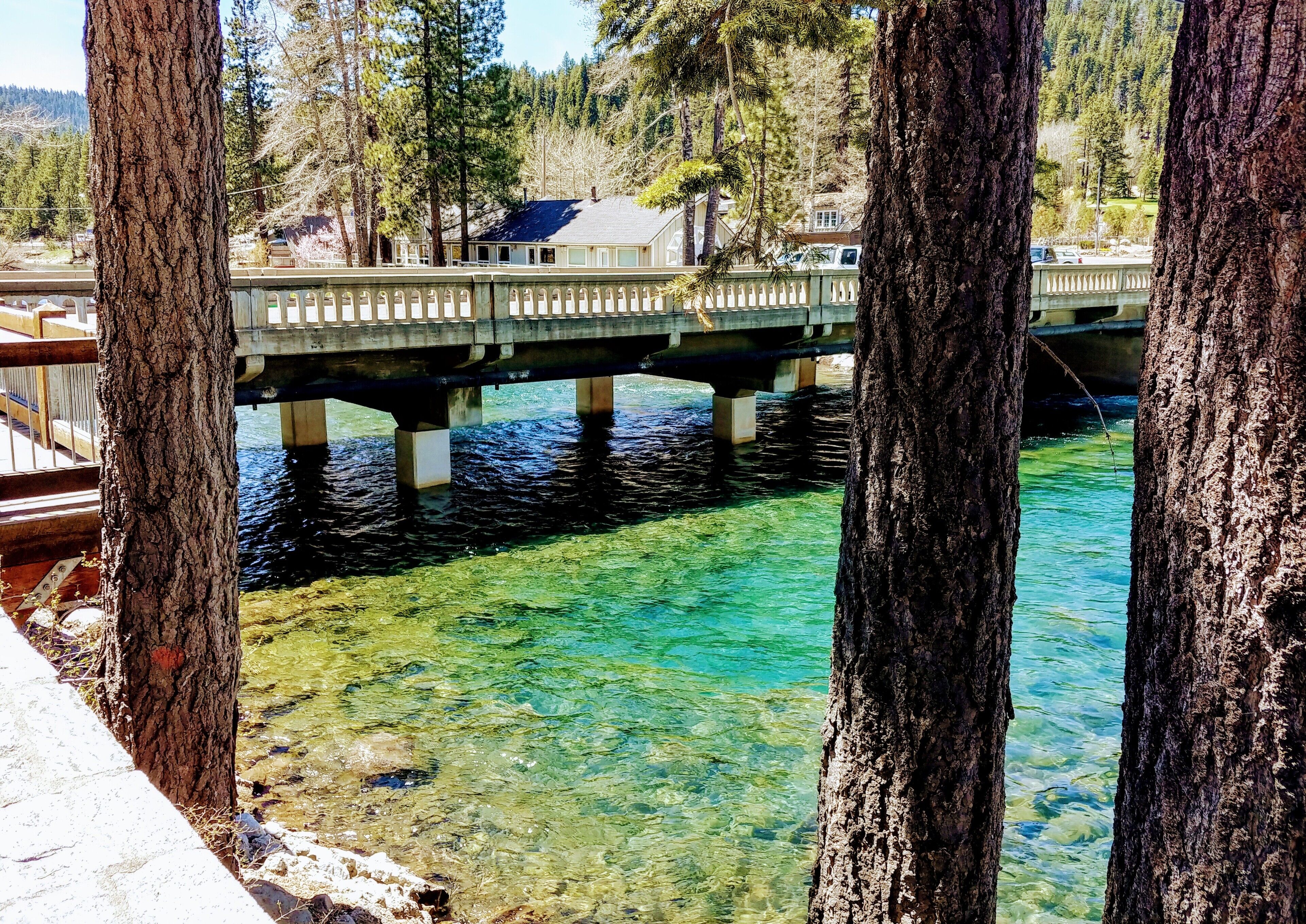 Un pont enjambant une rivière aux eaux claires, avec une maison en arrière-plan.