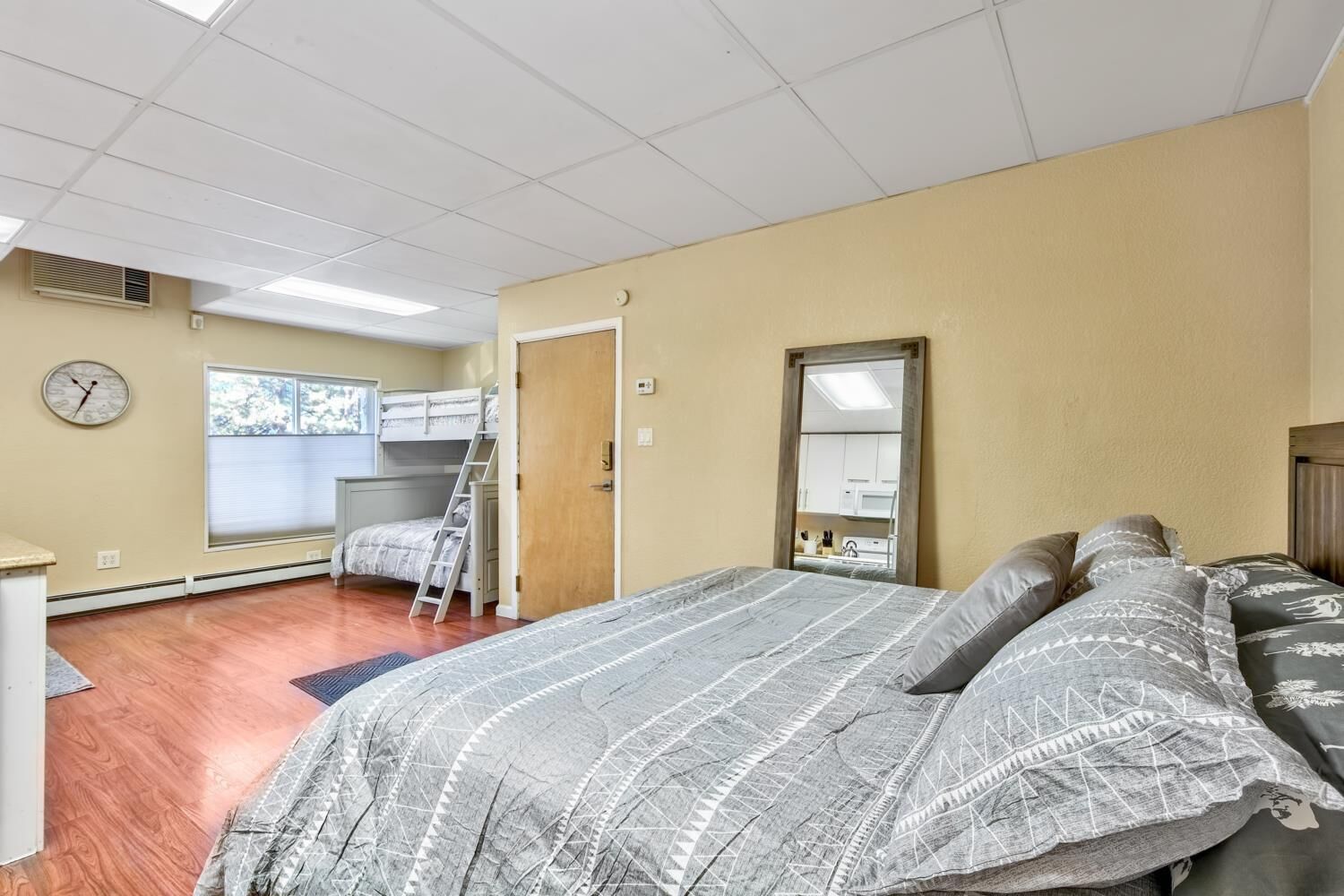 Ein Schlafzimmer mit Etagenbett, Schreibtisch, Stuhl, einem Fenster mit Jalousien, einer Uhr und einem Spiegel.