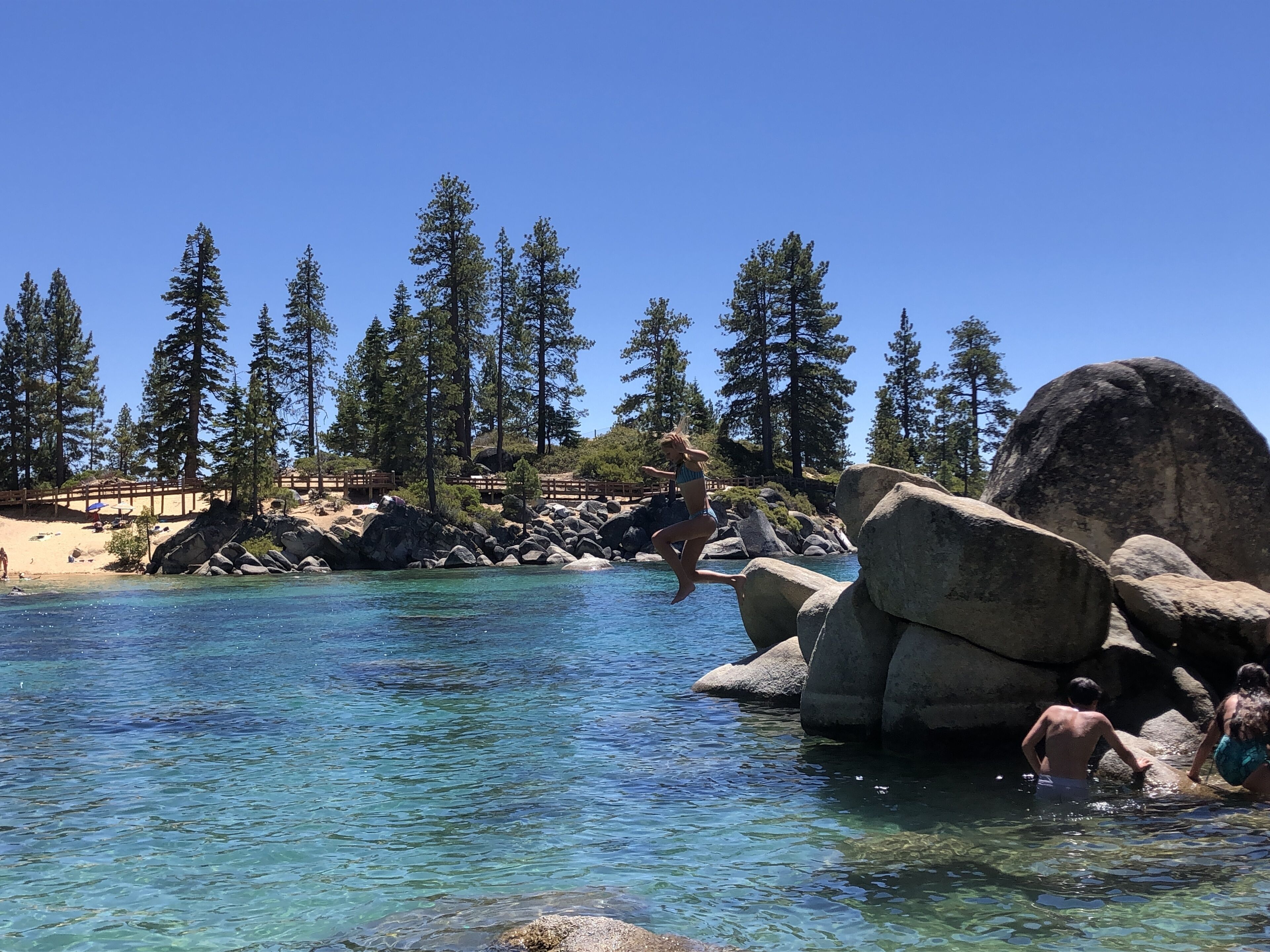 Piscina azul límpida rodeada por pedras grandes e árvores.