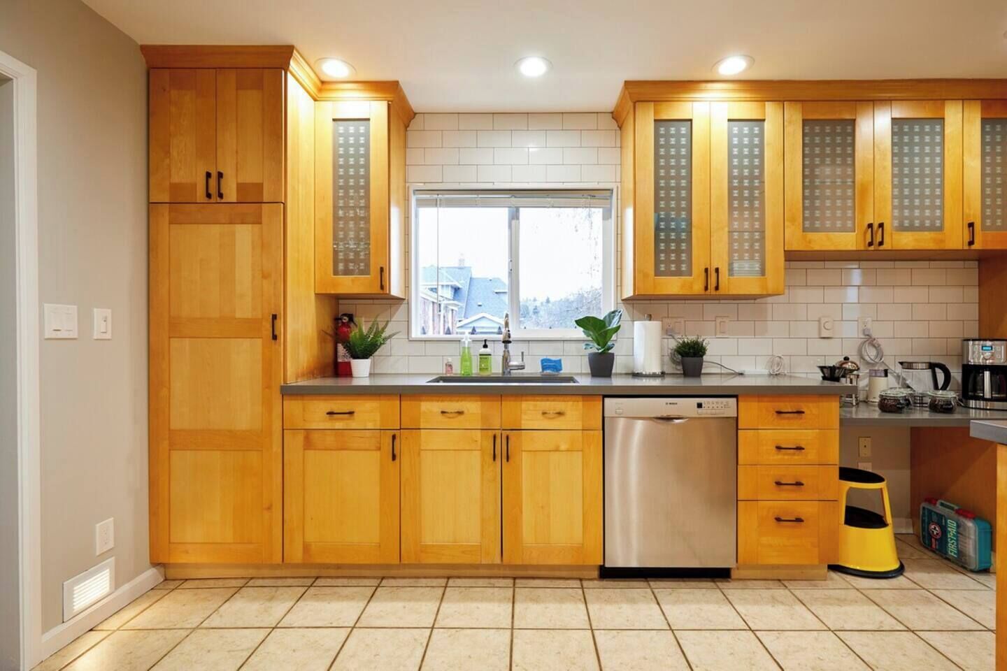 A modern kitchen with wooden cabinets, a stainless steel dishwasher, and a window providing natural light.