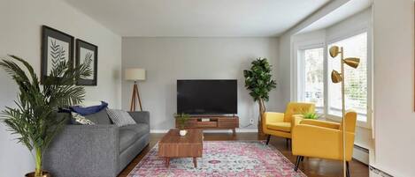 Una sala de estar moderna con un sofá gris, un sillón amarillo y un televisor de pantalla plana sobre un pedestal de madera.