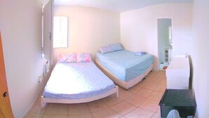 A small, bright room with two single beds, a white door, and a small desk with a chair.