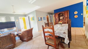 A dining area with a TV, wicker chairs, a table with a patterned tablecloth, and a blue accent wall.