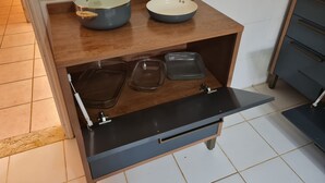 A kitchen with a wooden countertop, two pots, a frying pan, and a drawer with clear storage containers.