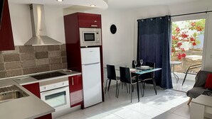 Una cucina compatta con forno, microonde e piano cottura integrati, un'area pranzo con tavolo e sedie, e vista su un giardino attraverso una finestra.