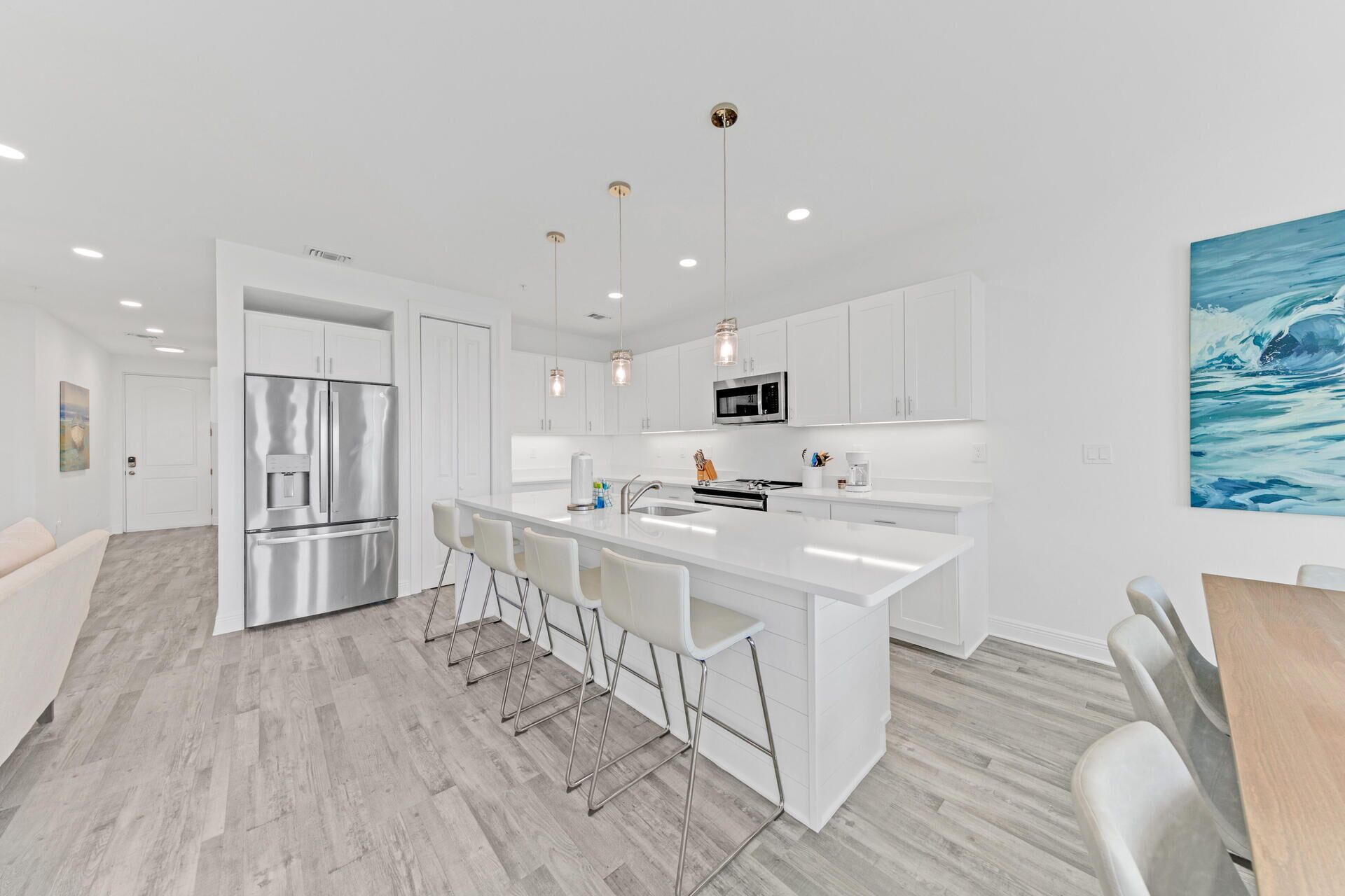 A modern kitchen with white cabinetry, stainless steel appliances, and a central island with bar stools.