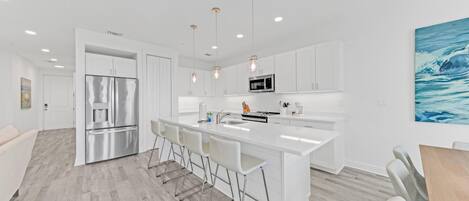 A modern kitchen with white cabinetry, stainless steel appliances, and a central island with bar stools.
