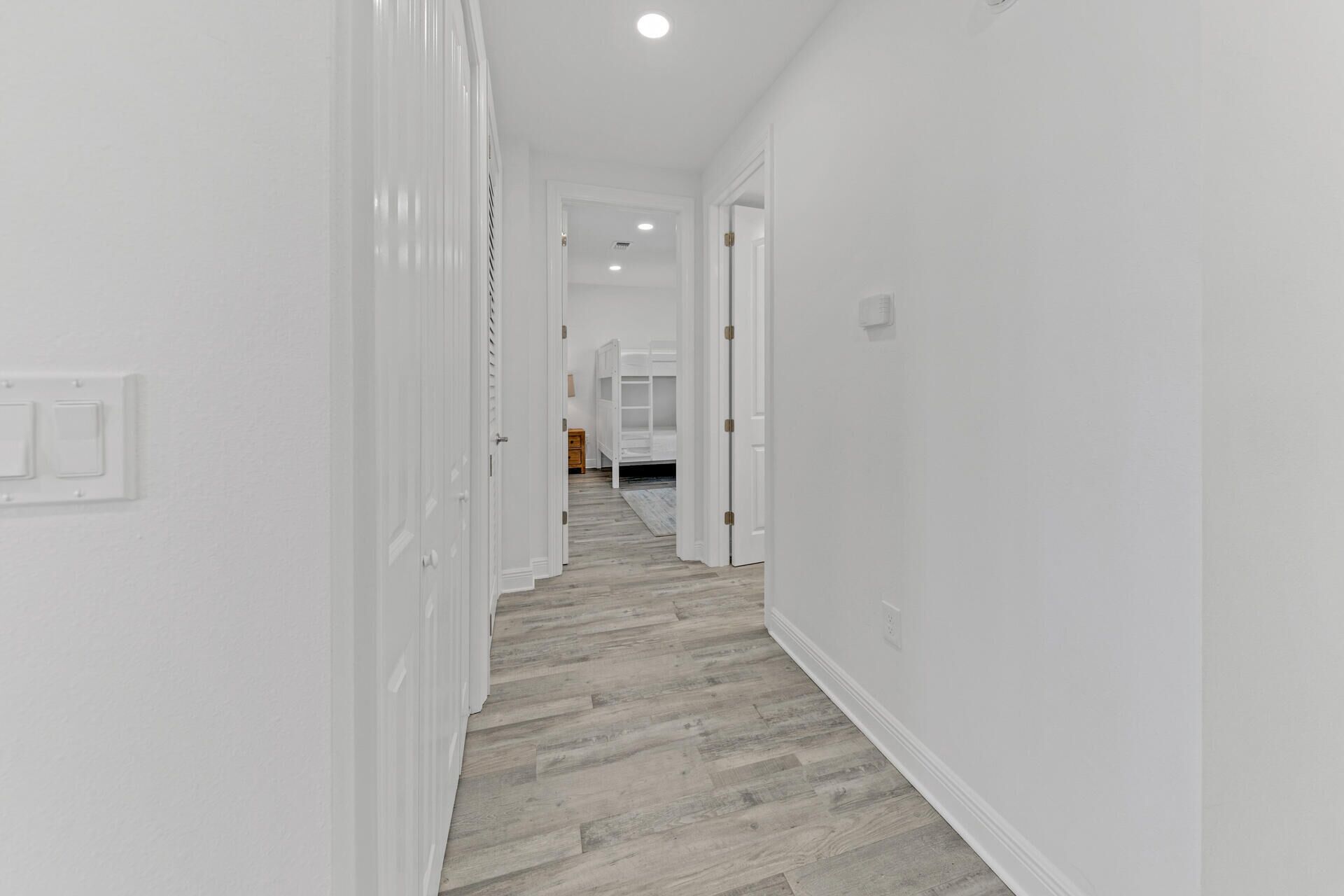 A hallway with white walls and wooden flooring leading to a bedroom with a bunk bed.
