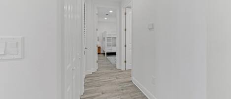A hallway with white walls and wooden flooring leading to a bedroom with a bunk bed.
