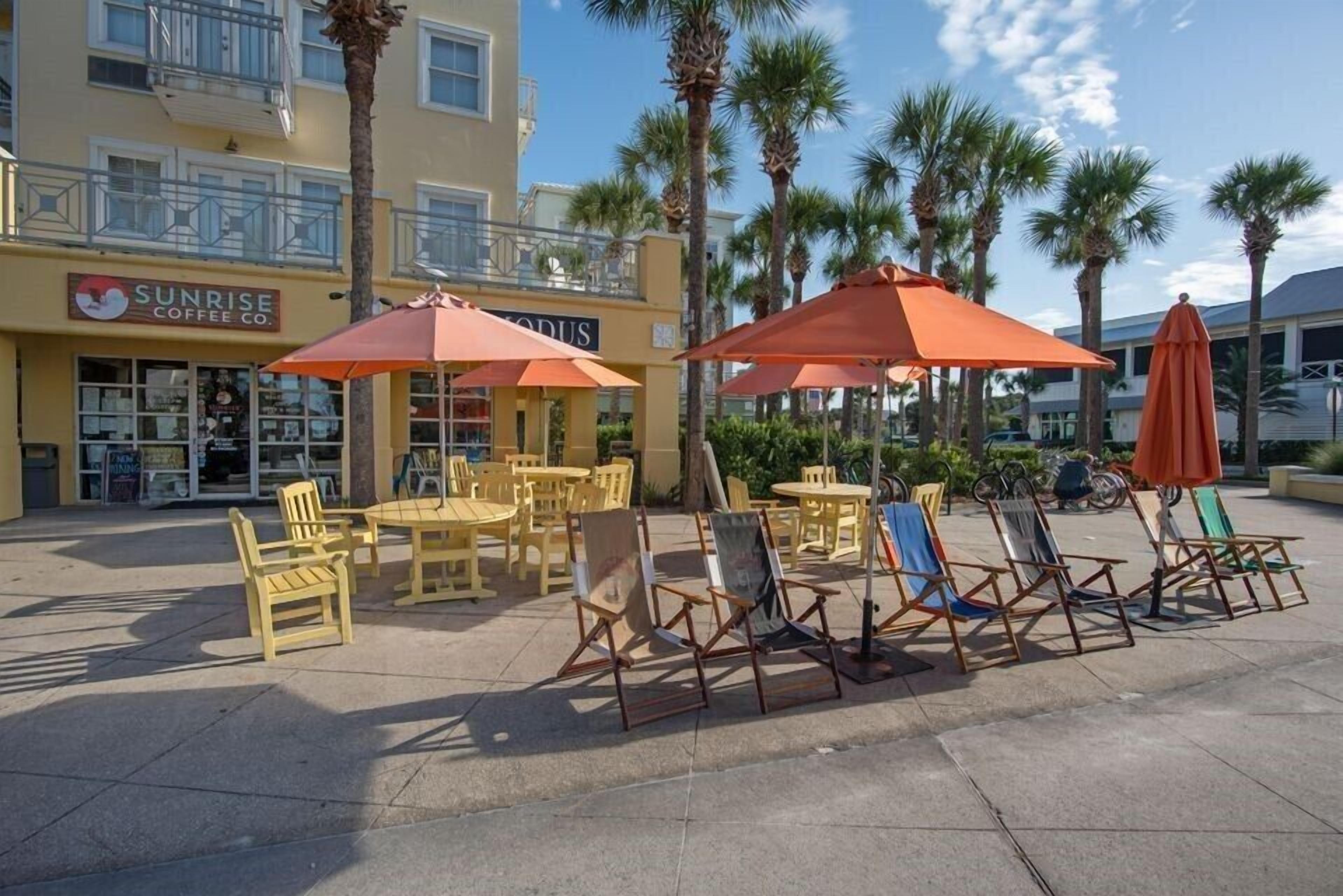 An outdoor seating area with yellow chairs and orange umbrellas, a coffee shop named Sunrise Coffee Co., and palm trees in the background.