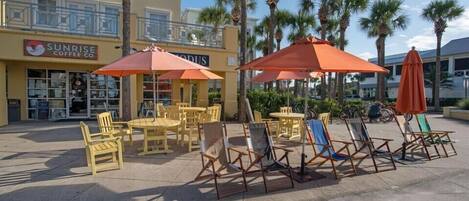 An outdoor seating area with yellow chairs and orange umbrellas, a coffee shop named Sunrise Coffee Co., and palm trees in the background.