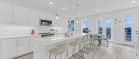 Una cocina moderna con armarios blancos, una isla grande con taburetes y vistas al exterior gracias a amplios ventanales.