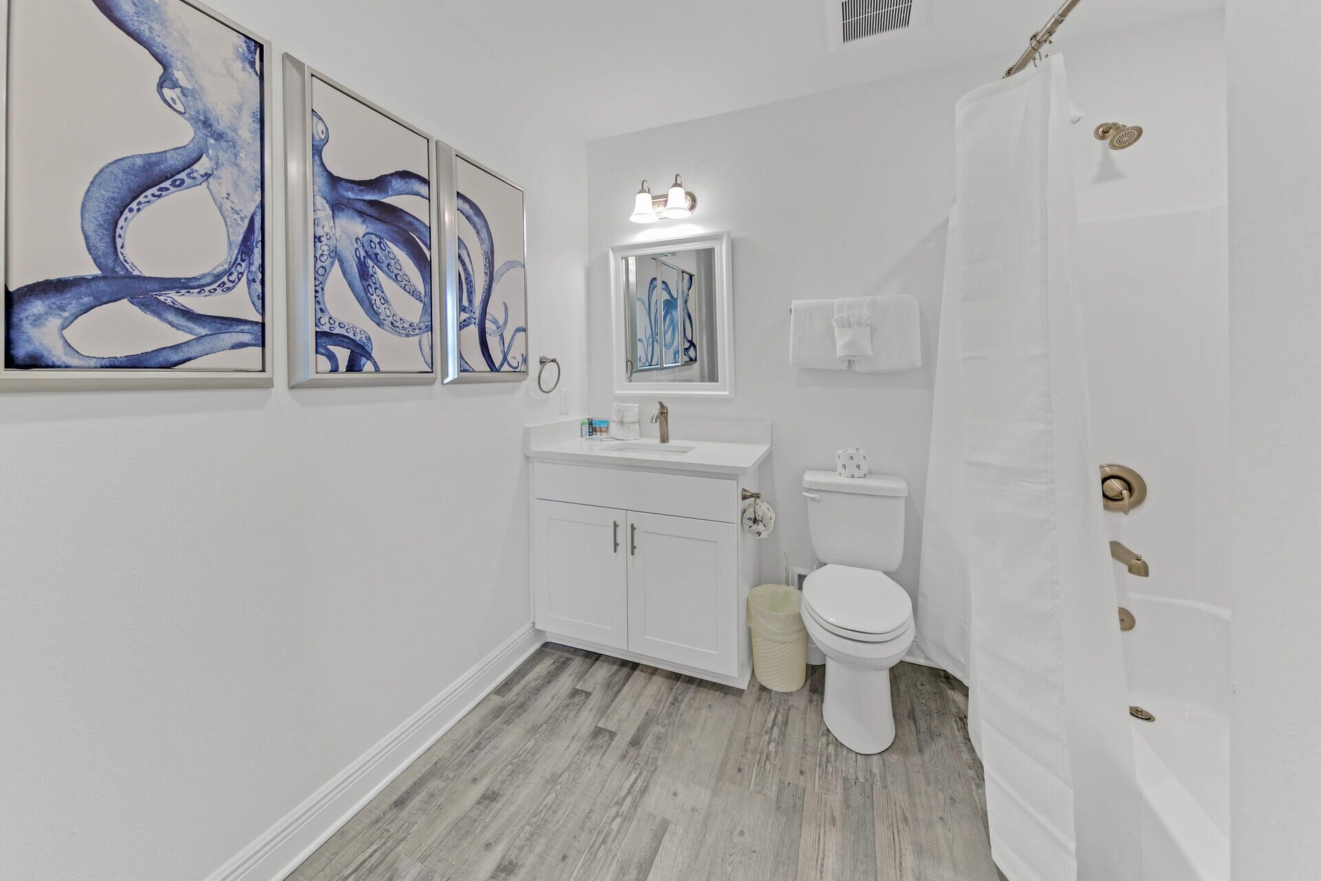 A bathroom with a white sink, toilet, and shower curtain. There are three framed artworks on the wall.