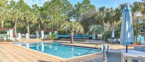 A swimming pool with lounge chairs and umbrellas, surrounded by palm trees and a clear sky.