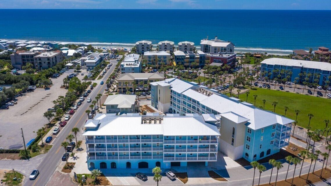 A coastal hotel with multiple buildings, a parking lot, and a view of the ocean.