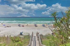 Una playa con un paseo marítimo de madera que conduce a la orilla, rodeada de vegetación.