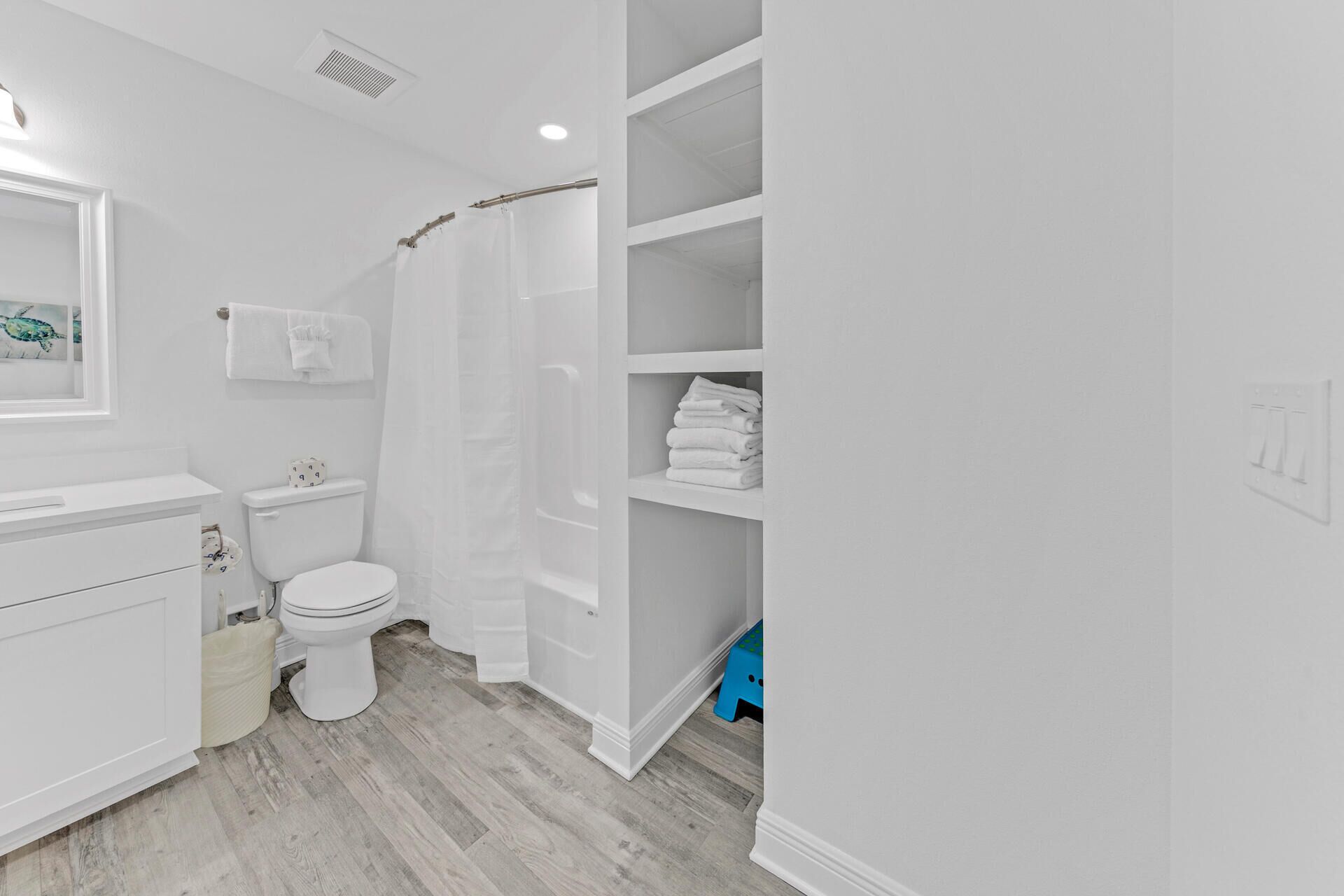 Une salle de bain comprenant des toilettes, un lavabo, un rideau de douche et une étagère avec des serviettes pliées.