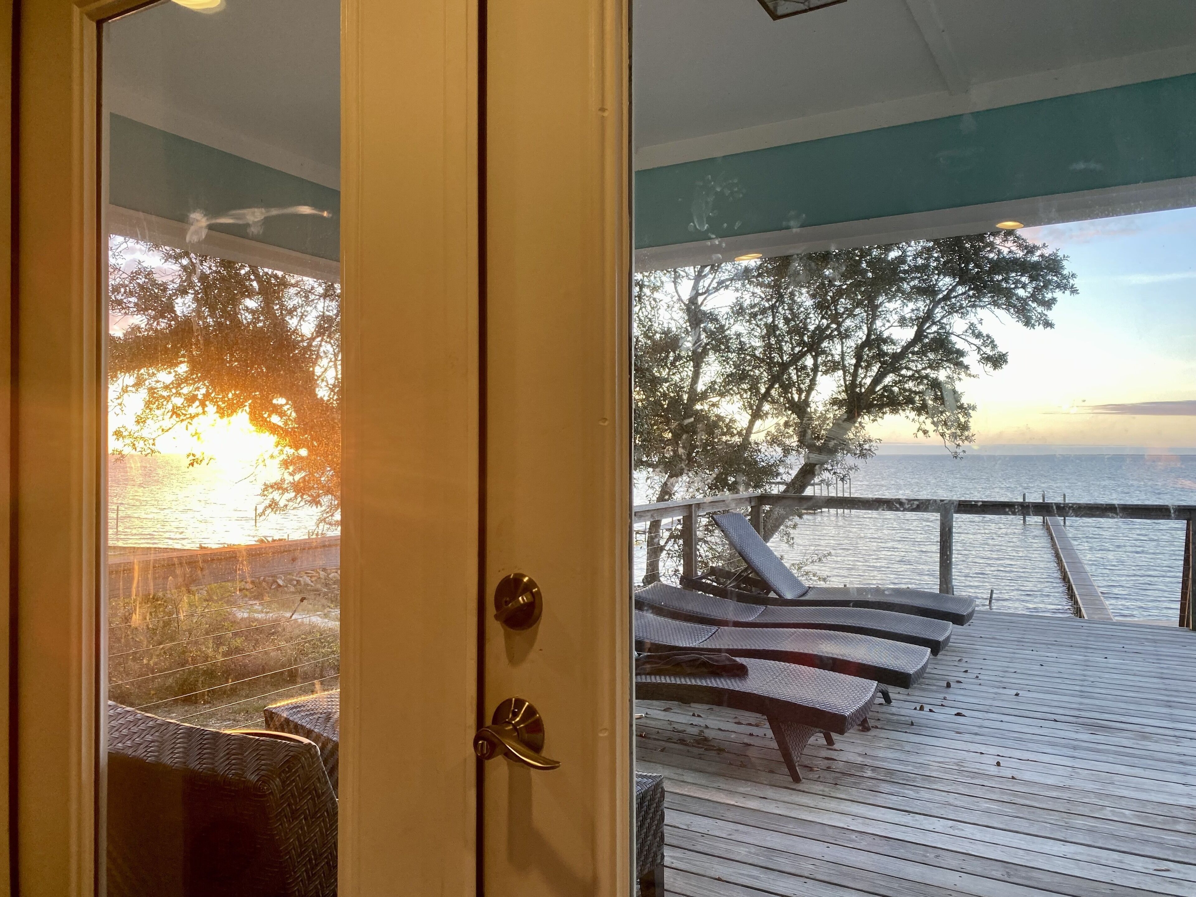 A wooden deck with lounge chairs overlooking a body of water and a sunset.