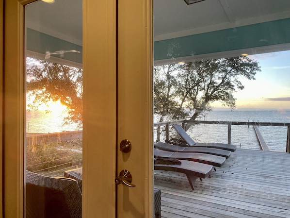 En træterrasse med liggestole med udsigt over vand og en solnedgang.