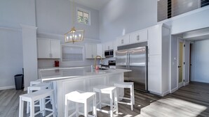 A modern kitchen with white cabinetry, a large island with bar stools, stainless steel appliances, and a pendant light. - Deer Brook Lake House (Jamestown)