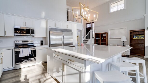 A modern kitchen with white cabinetry, stainless steel appliances, and a central island with bar stools. - Deer Brook Lake House (Jamestown)