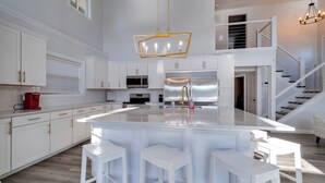 A modern kitchen with white cabinetry, a large island with bar stools, stainless steel appliances, and a staircase leading to an upper level. - Deer Brook Lake House (Jamestown)