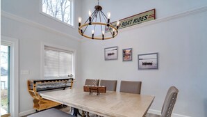 A dining area with a large wooden table, cushioned benches, and a chandelier. - Deer Brook Lake House (Jamestown)