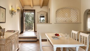 Un comedor con una mesa y sillas blancas, vistas al exterior y una escalera que lleva a un balcón.