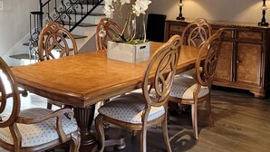 A dining area with a wooden table and chairs, a staircase with black railings, and a cabinet with lamps. - Lakefront 3 Bedroom house with breath taking views (Agoura Hills)