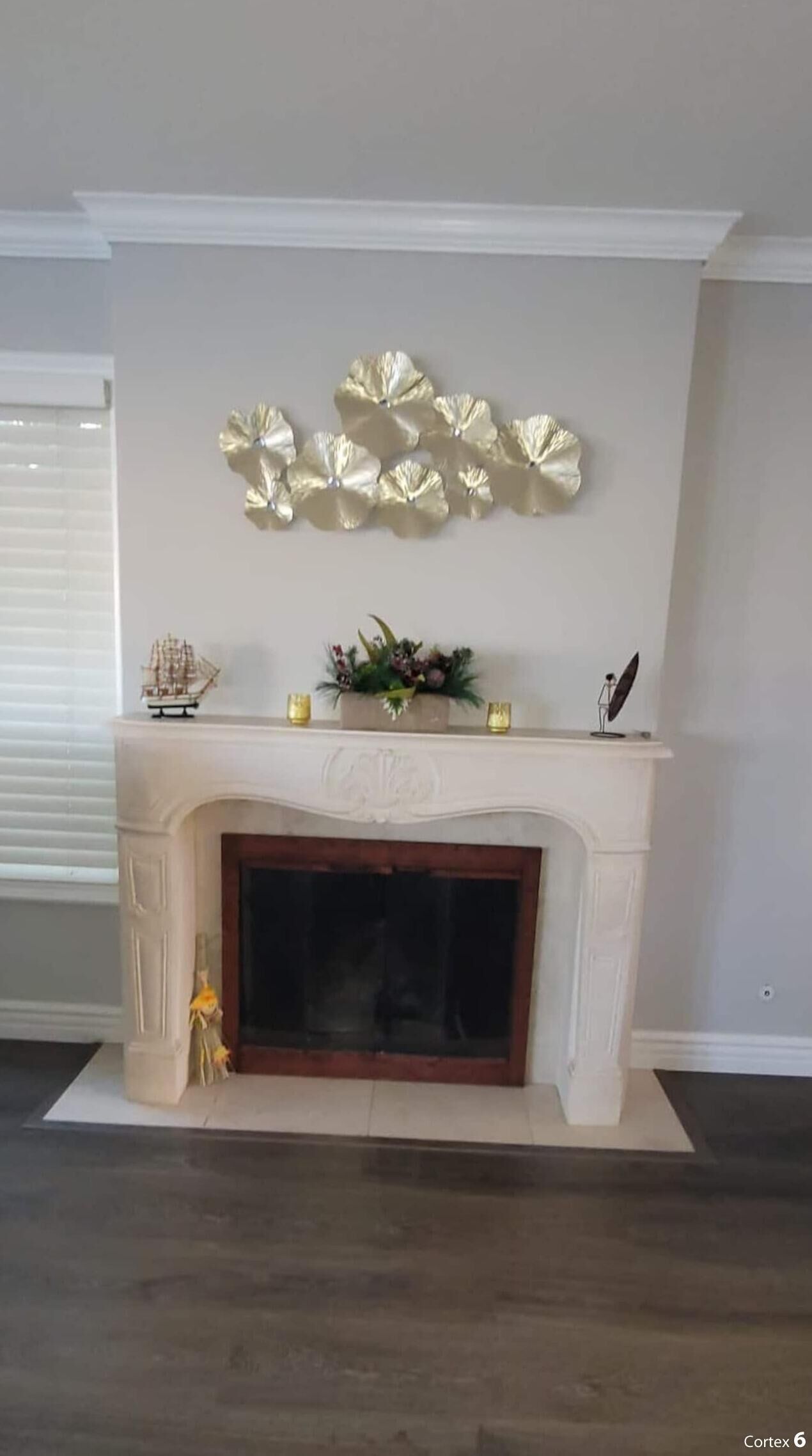 A fireplace with a mantel decorated with a leaf-like sculpture, a ship model, and candles.