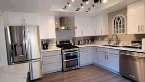 A modern kitchen with stainless steel appliances, white cabinetry, and a wooden floor. - Lakefront 3 Bedroom house with breath taking views (Agoura Hills)