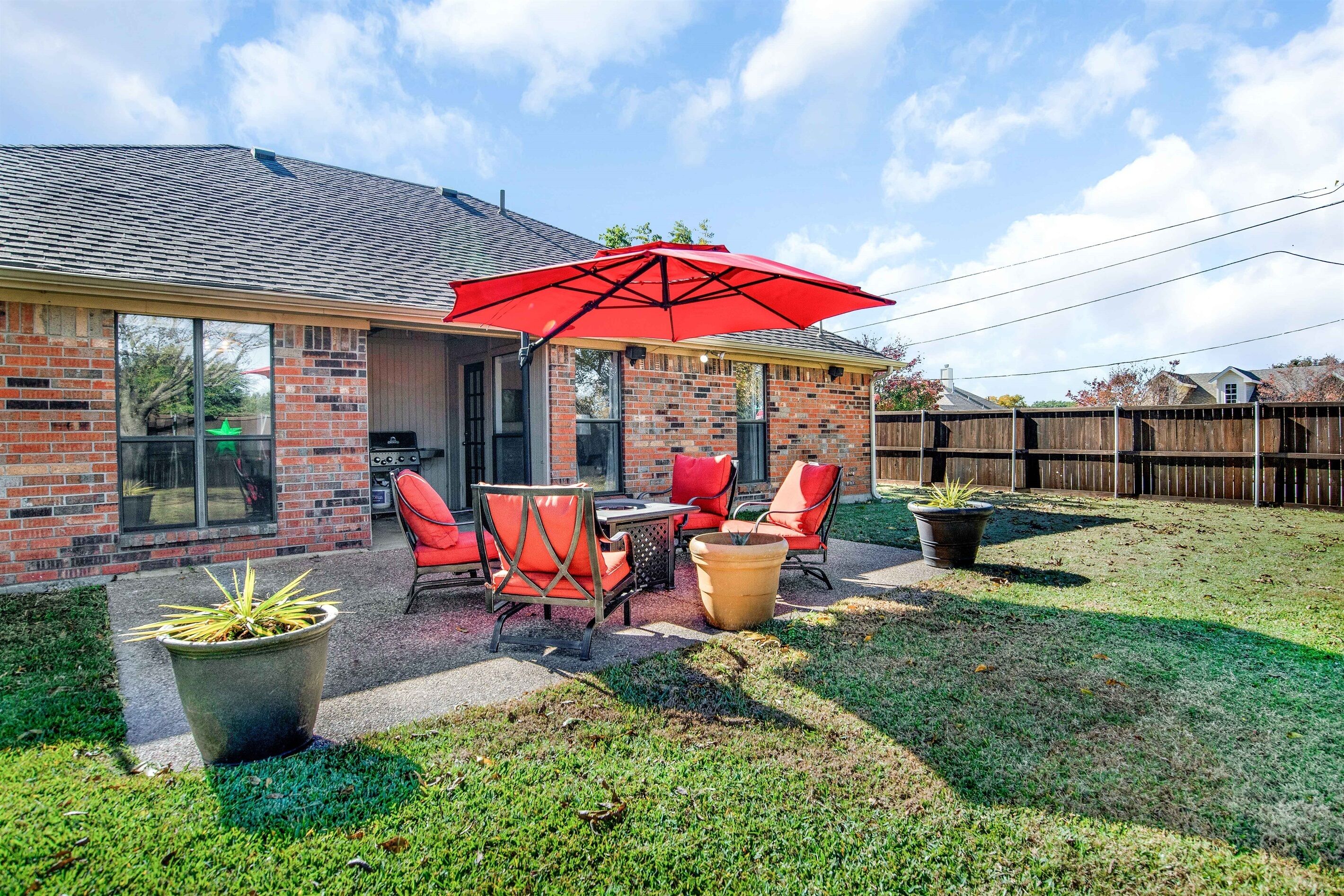 A backyard patio with a brick house, outdoor furniture, and a red umbrella.
