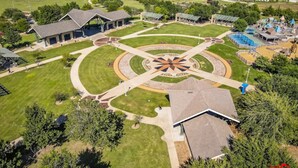 Luftaufnahme eines Parks mit einer zentralen, kreisförmigen Rasenfläche, umgebenden Gebäuden und Spielgeräten.