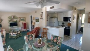 Una sala de estar con televisor, una mesa de comedor y una cocina al fondo.