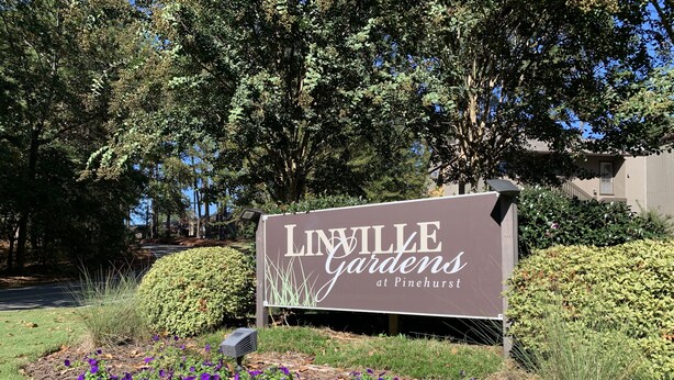 Señal de 'LIVILLE Gardens at Pinehurst' que muestra un jardín con flores púrpuras y un césped bien cuidado.