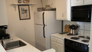 Una cocina con armarios blancos, un microondas negro, un lavamanos de acero inoxidable y una estufa negra.