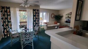 Un espacio habitable compacto con comedor, sofá, una mesita, ventilador de techo y cocina con lavaplatos.