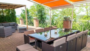 An outdoor patio with a glass-top table, wicker furniture, and a brick fireplace. - Sant'Evasio by Interhome (Ovada)