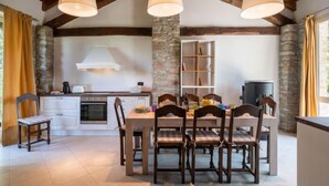 A rustic kitchen with exposed beams, a stone column, and a dining area with wooden chairs and a table. - Sant'Evasio by Interhome (Ovada)