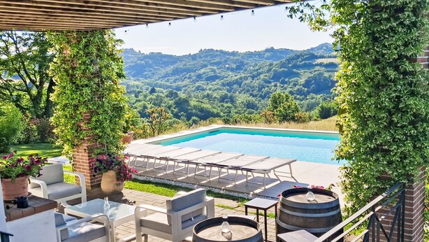An outdoor pool area with lounge chairs and tables, surrounded by greenery and hills. - Sant'Evasio by Interhome (Ovada)