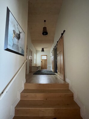 Eine Holztreppe führt zu einer Tür am Ende eines Ganges, an der Wand hängt ein gerahmtes Bild.