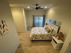 Ein Schlafzimmer mit Bett, Nachttisch, Deckenventilator, Fenster mit Aussicht und einer Tür zum Balkon.