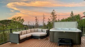 A wooden deck with a sectional sofa and a hot tub.