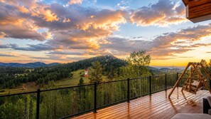 A wooden deck with a swing chair and a view of a forested landscape. - Colorado Mountain Villa (Morrison)