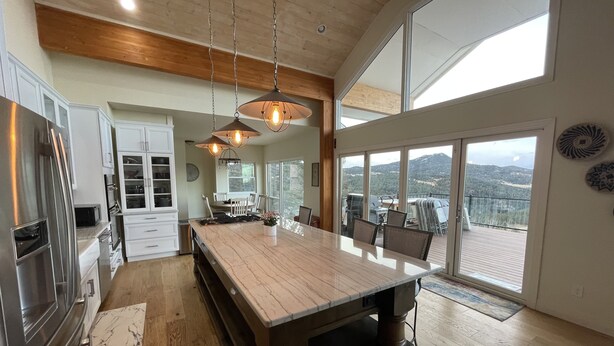 A modern kitchen with a large island, stainless steel appliances, and a dining area with a view of the outdoors.