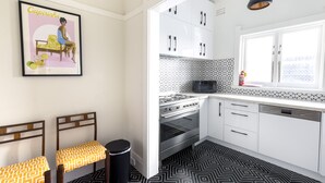 A kitchen with white cabinets, a black and white patterned floor, a stove, oven, microwave, and a window with a view. - Stylish Bondi Beach pad moments from sand & surf (Bondi Beach)