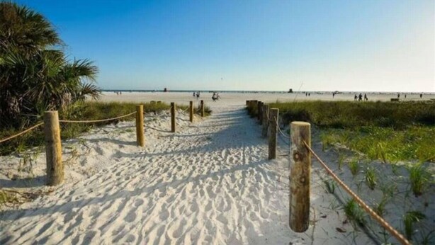 Un sendero arenoso en la playa con postes y cuerdas de madera, que lleva al océano.