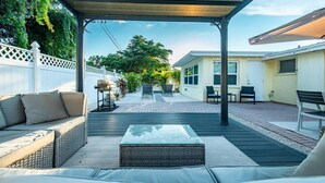 Un patio techado con mobiliario exterior, una parrilla y una vista de una casa al fondo.